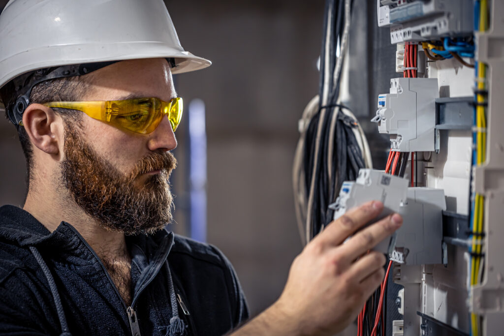 A male electrician works in a switchboard with an electrical connecting cable.